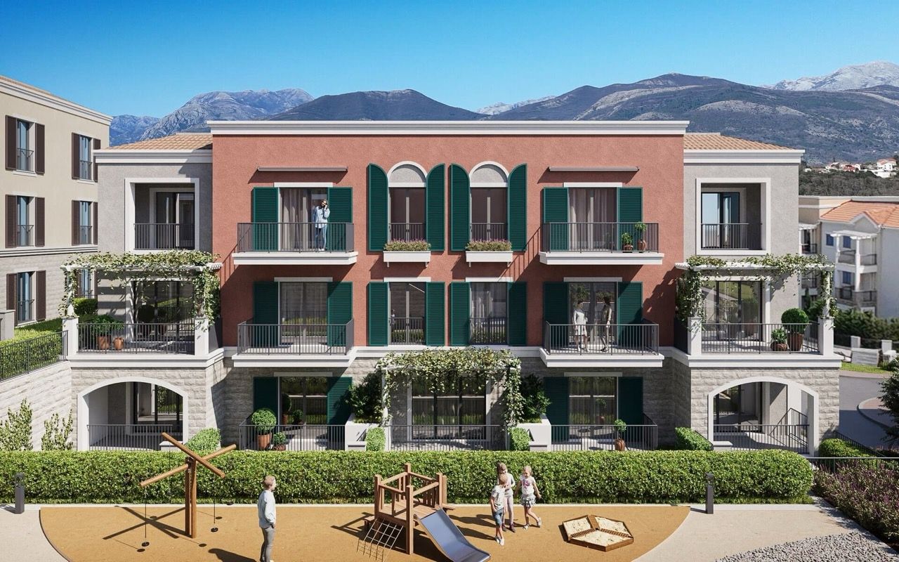 Facade of a residential complex in Luštica Bay, Radovići, Montenegro: terraces with green shutters and a playground by the building.