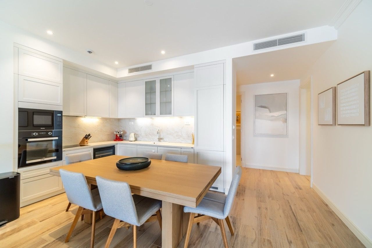 Modern kitchen in an apartment in Luštica Bay, Radovići, Montenegro: light-colored cabinetry, wooden table, and built-in appliances.