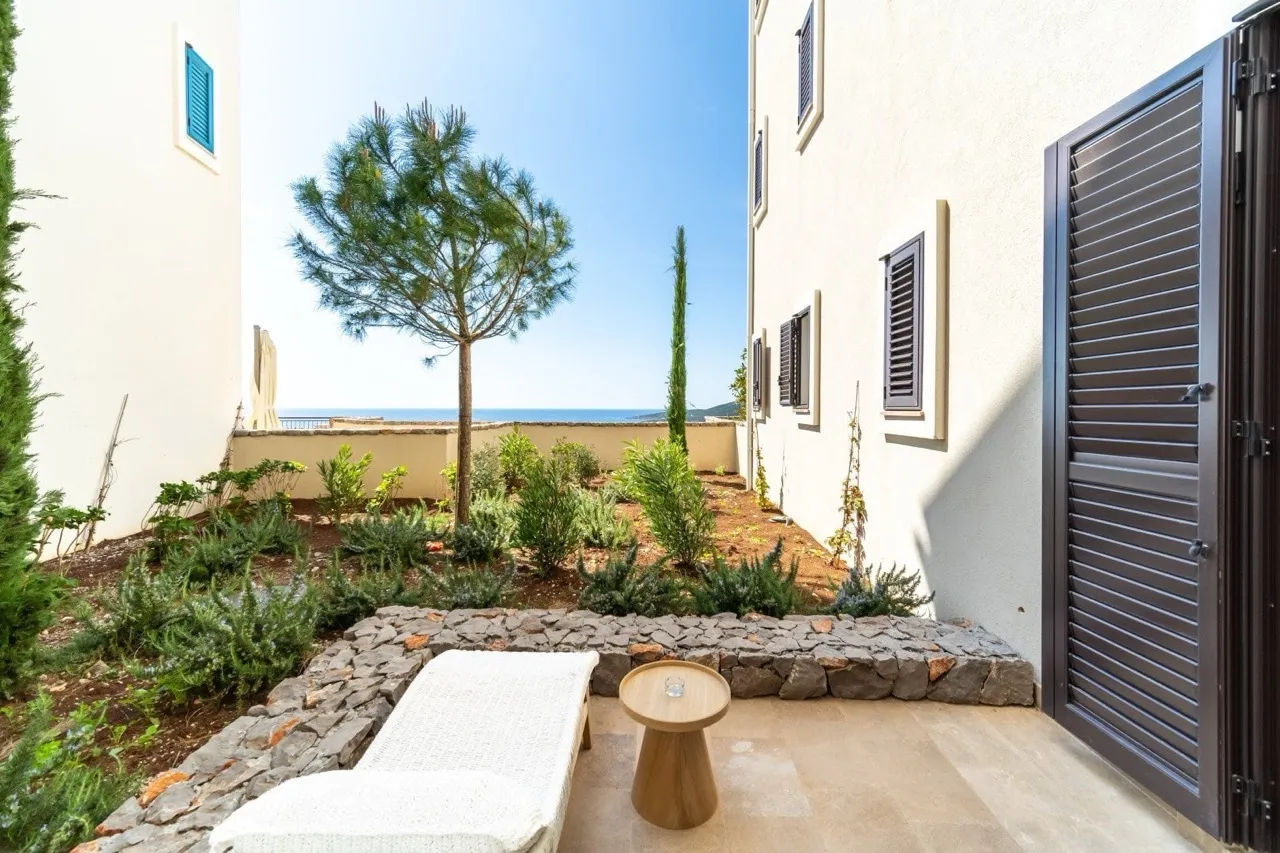 Open terrace courtyard with stone border, white lounger, wooden table, and garden plants overlooking the sea.