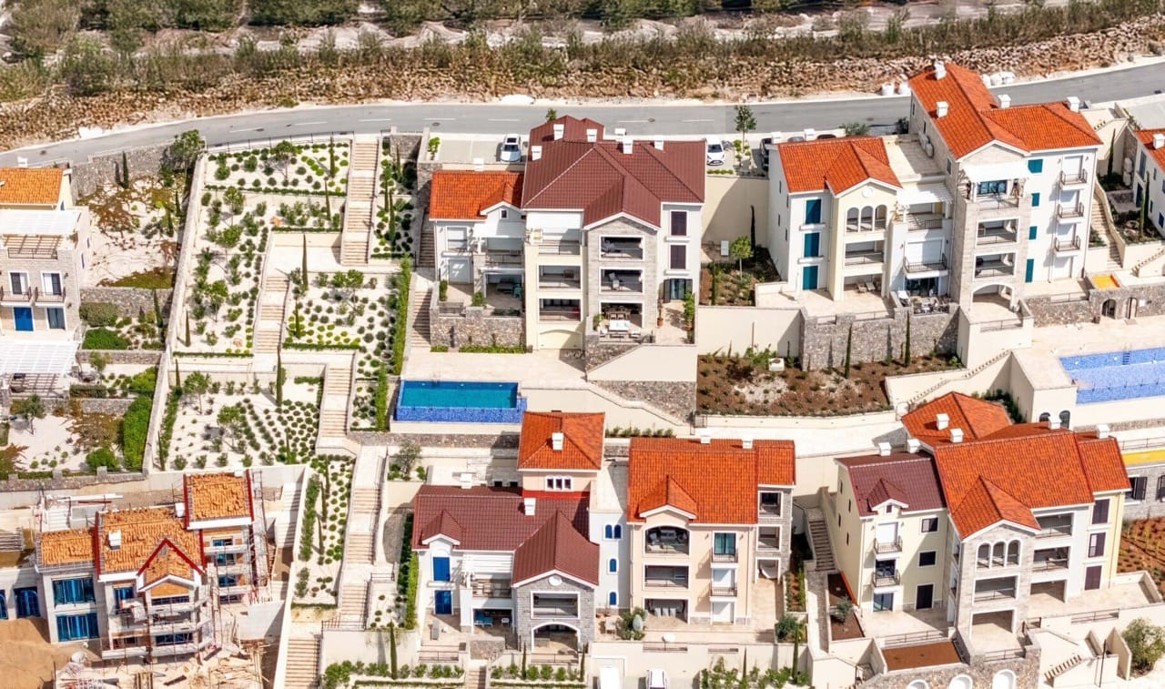 Aerial view of the Lustica Bay residential complex in Radovici, Montenegro: villas with red roofs, terraces, and swimming pools.