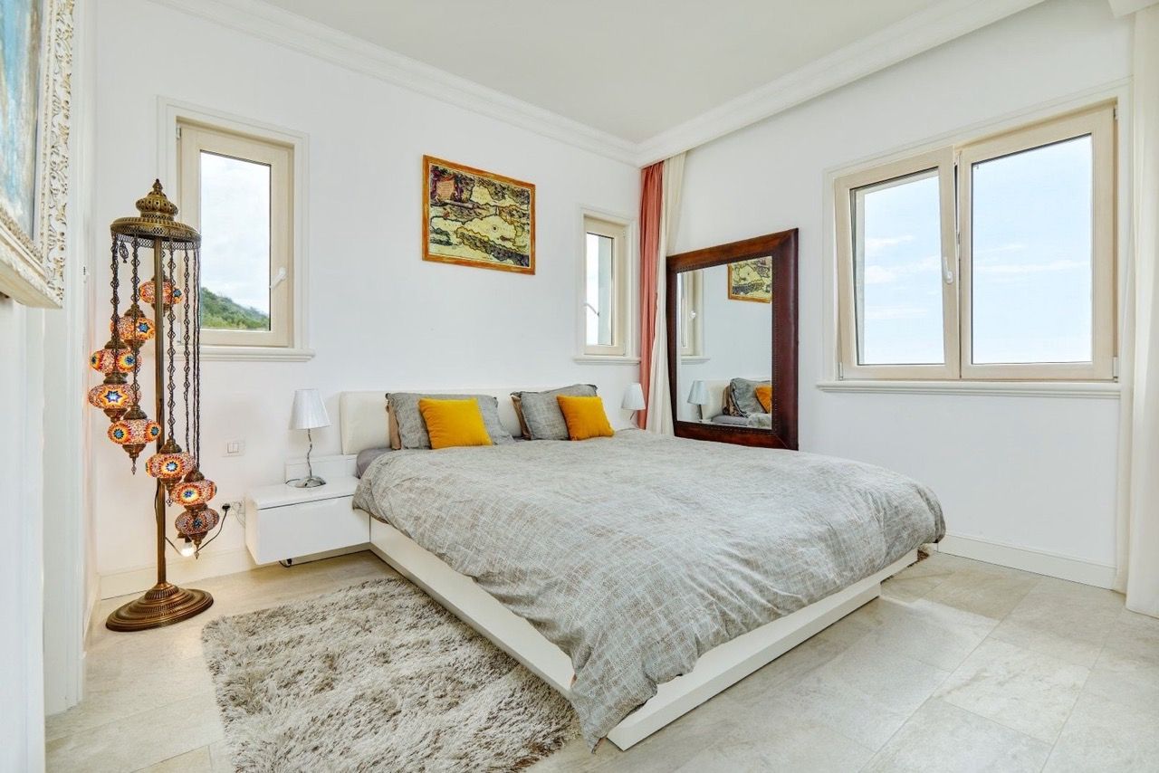 Bright bedroom in an apartment in Lustica Bay, Radovici, Montenegro: double bed, oriental floor lamp, and a view from the windows.