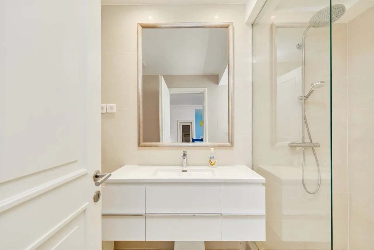 Modern bathroom featuring a white vanity sink, large framed mirror, and a glass-enclosed shower area with chrome fixtures.