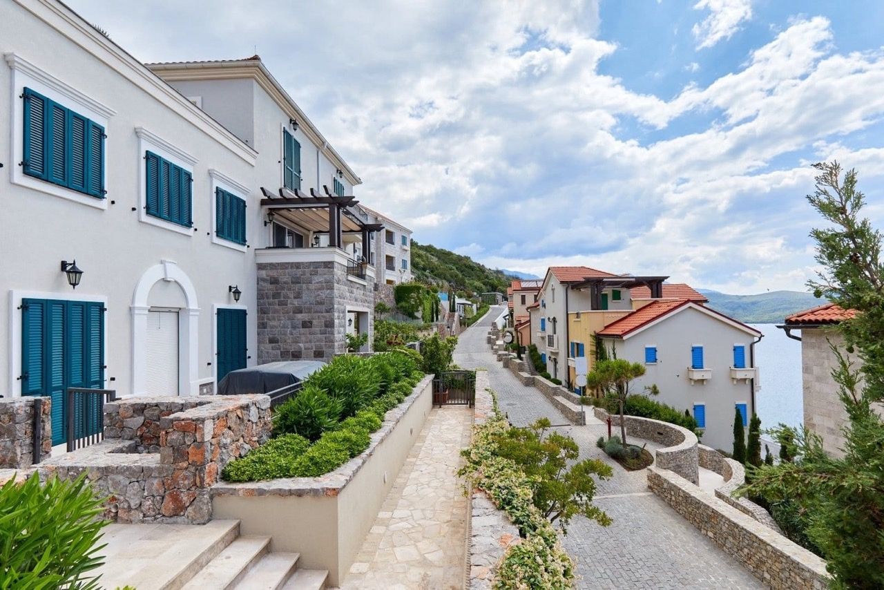 Street of the luxury Lustica Bay residential complex in Radovici, Montenegro: stone houses with blue shutters and sea view.