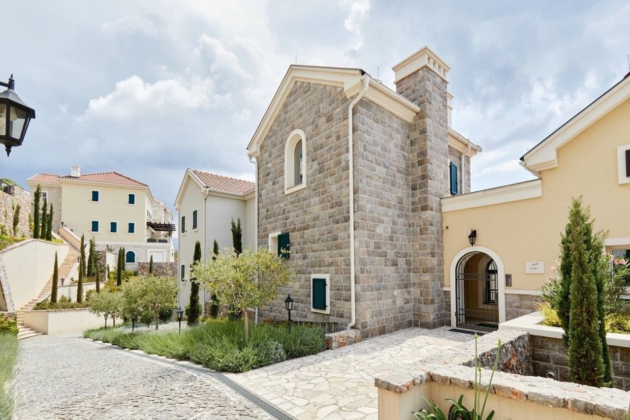 Facade of a stone villa in Mediterranean style in Luštica Bay, Radovići, Montenegro, with landscaped grounds.