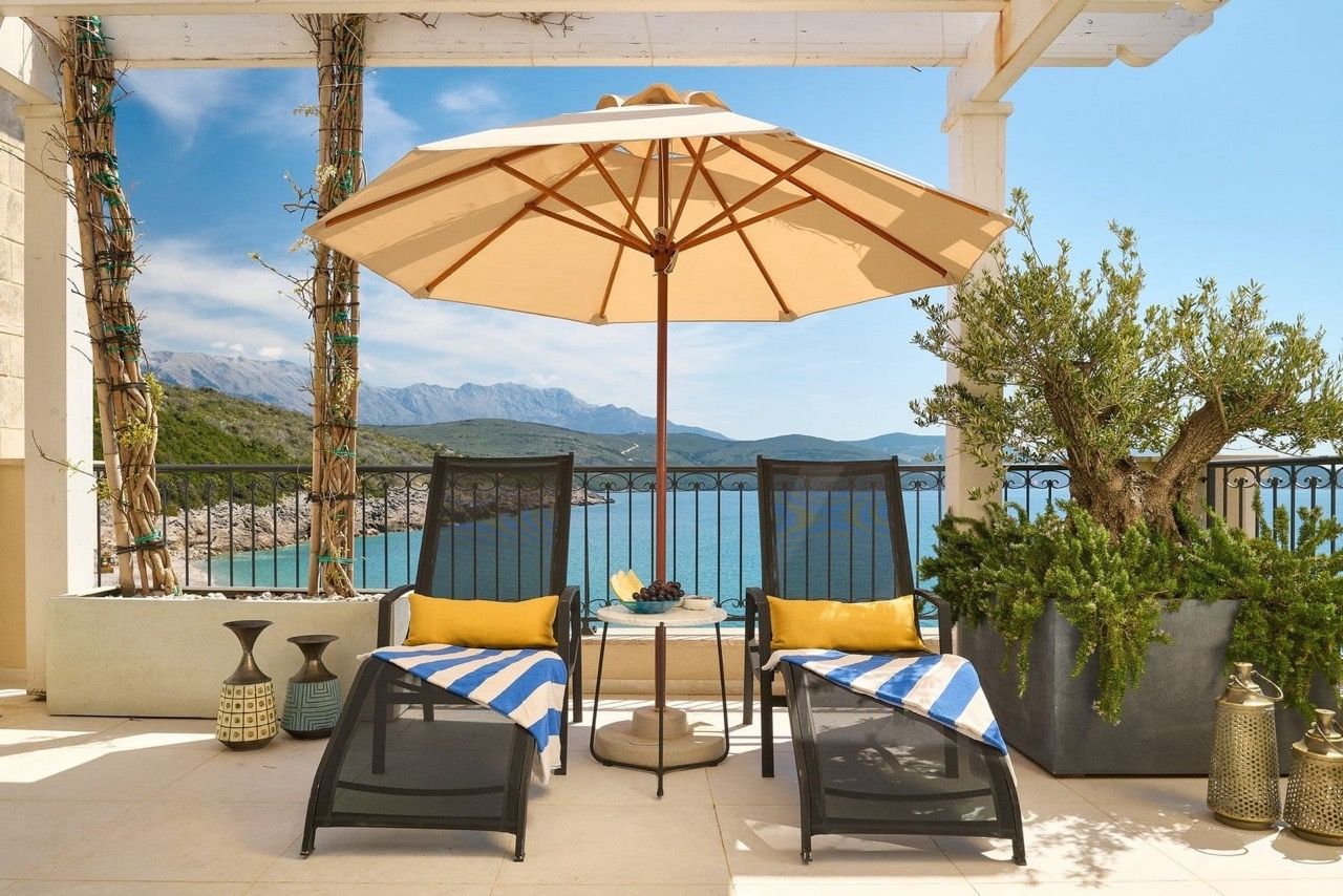 Terrace with sun loungers and an umbrella in Luštica Bay, Radovići, Montenegro: sea and mountain views, stylish outdoor furniture for relaxation.