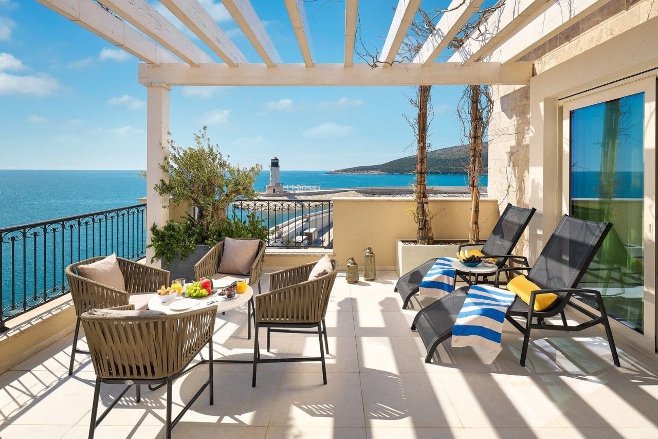 Apartment terrace in Luštica Bay, Radovići, Montenegro: sea view, lighthouse, wicker furniture, and sun loungers under a pergola.