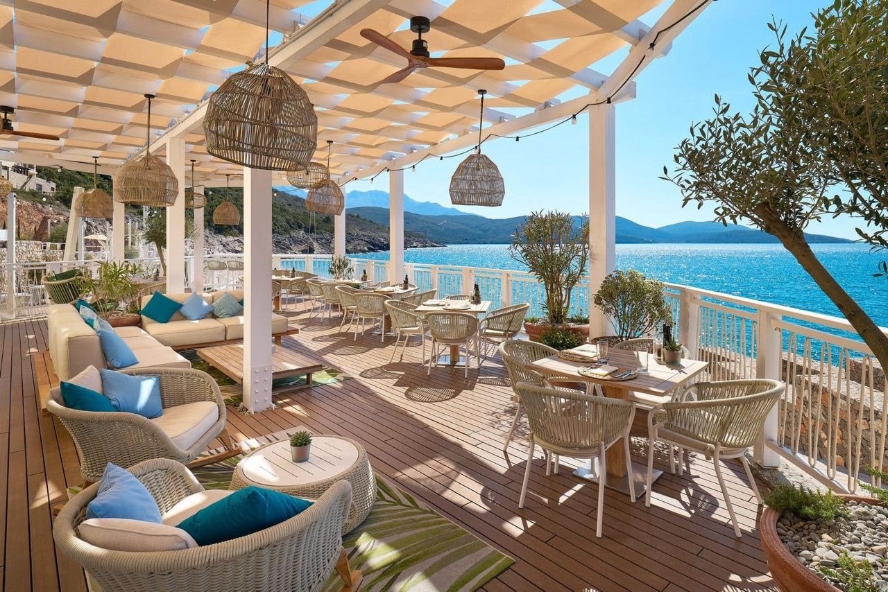 Restaurant terrace in Luštica Bay, Radovići, Montenegro: wicker furniture, canopy, sea and mountain view.