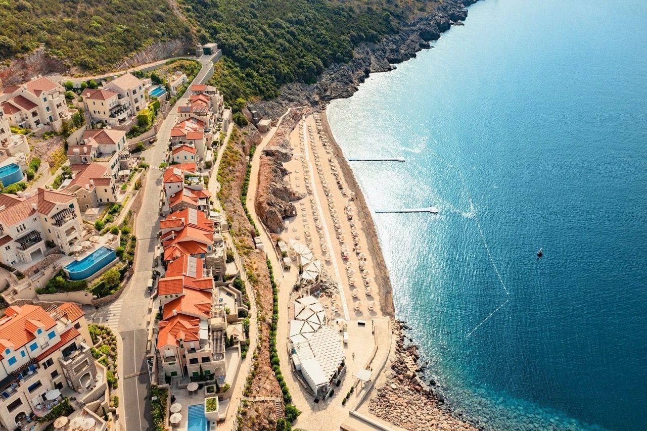 Aerial view of the luxury Lustica Bay complex in Radovići, Montenegro: private beach, villas, and the sea.