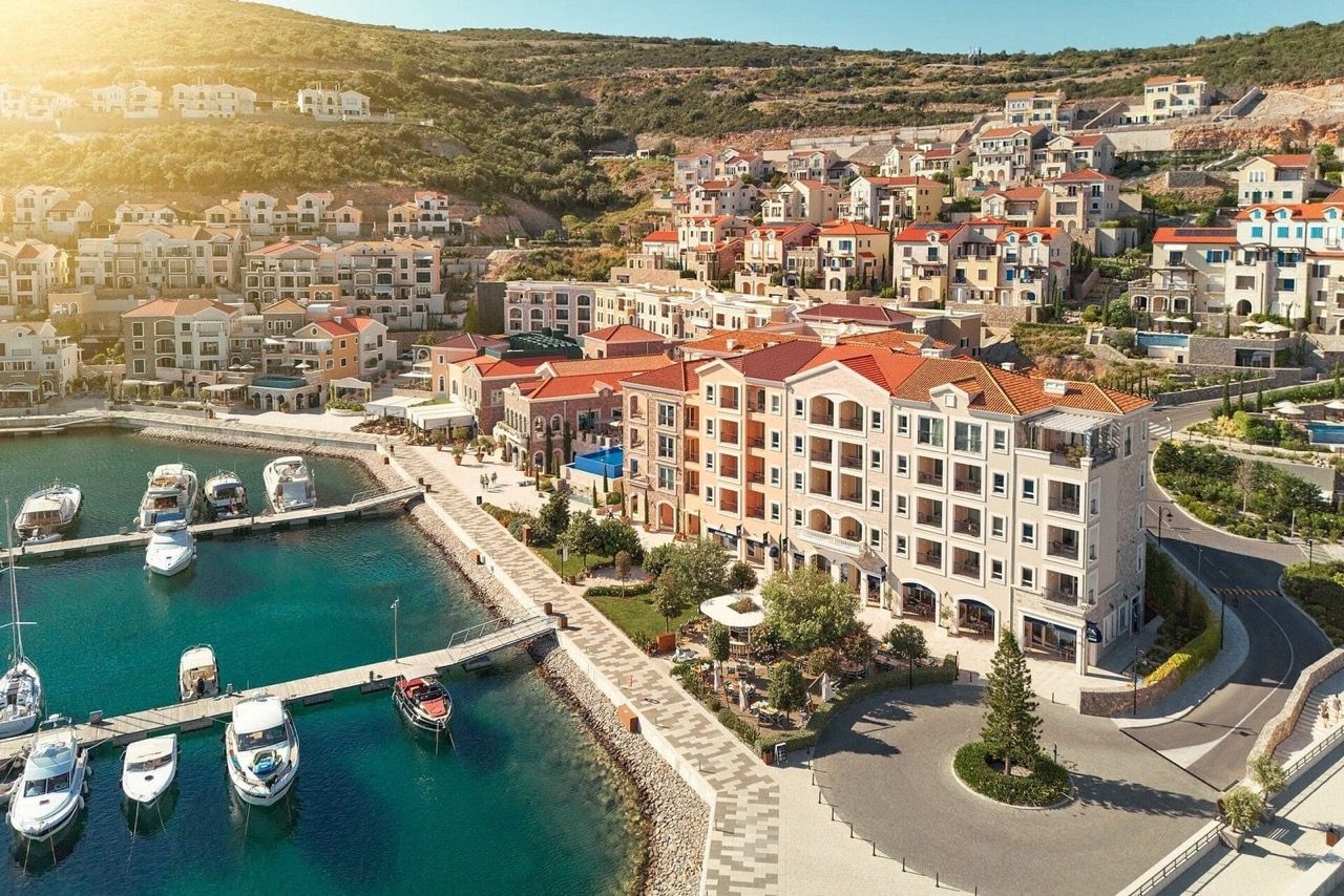 Aerial view of the luxury Lustica Bay residential complex in Radovici, Montenegro: waterfront promenade, yacht marina, and apartments.