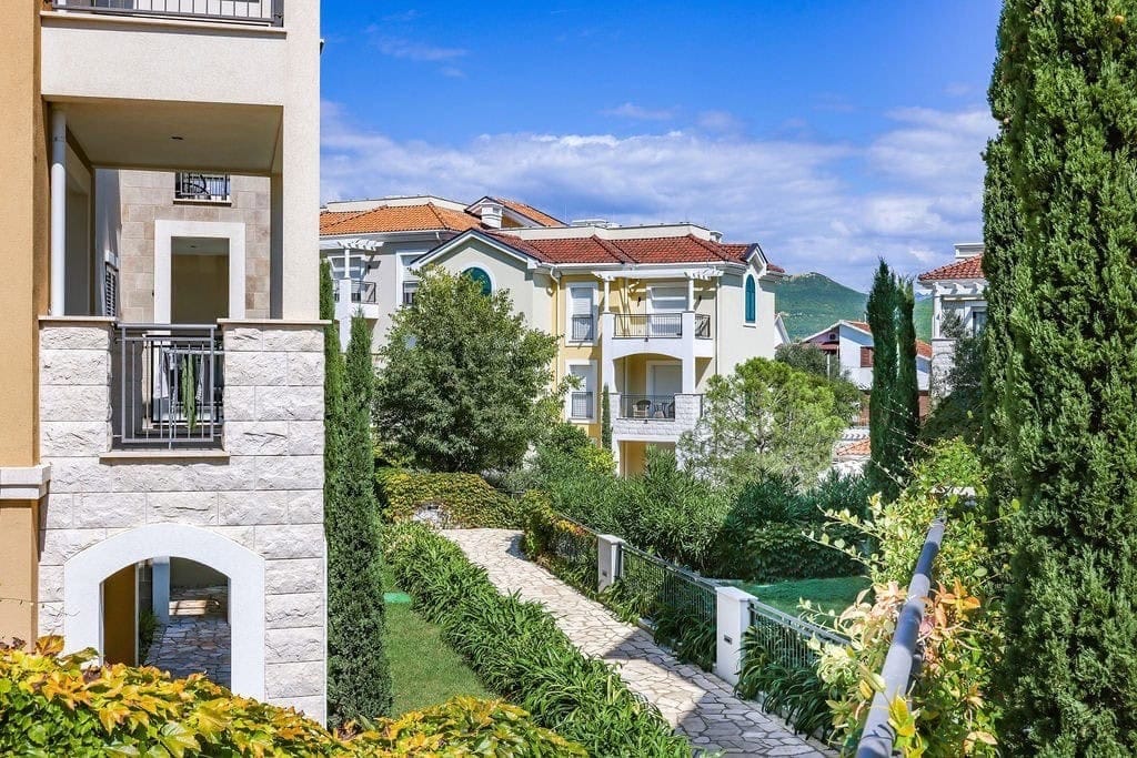 View of modern residential buildings with terraces in the Luštica Bay complex, Radovići, Montenegro, with a green garden and pathways.