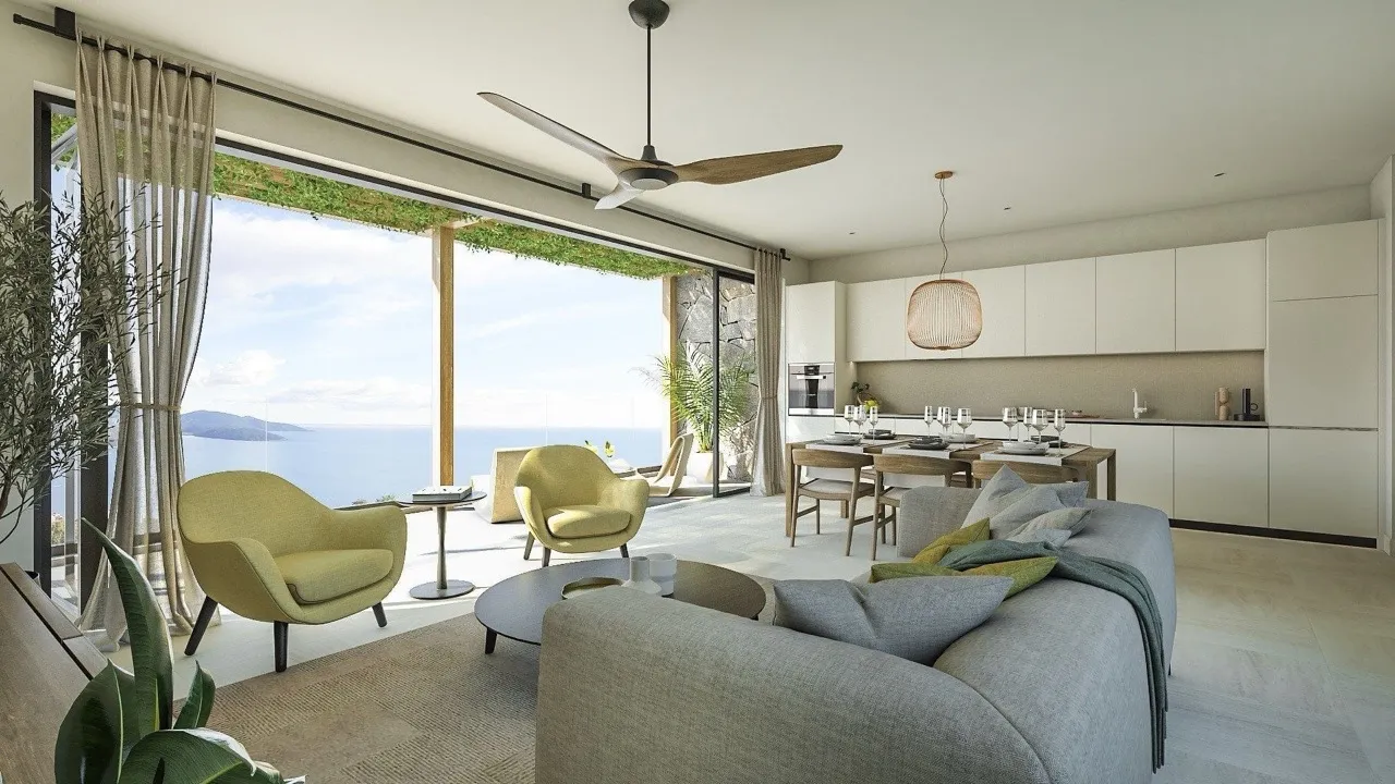 Modern living room with a grey sofa, yellow chairs, and an open kitchen near a large window overlooking the sea.