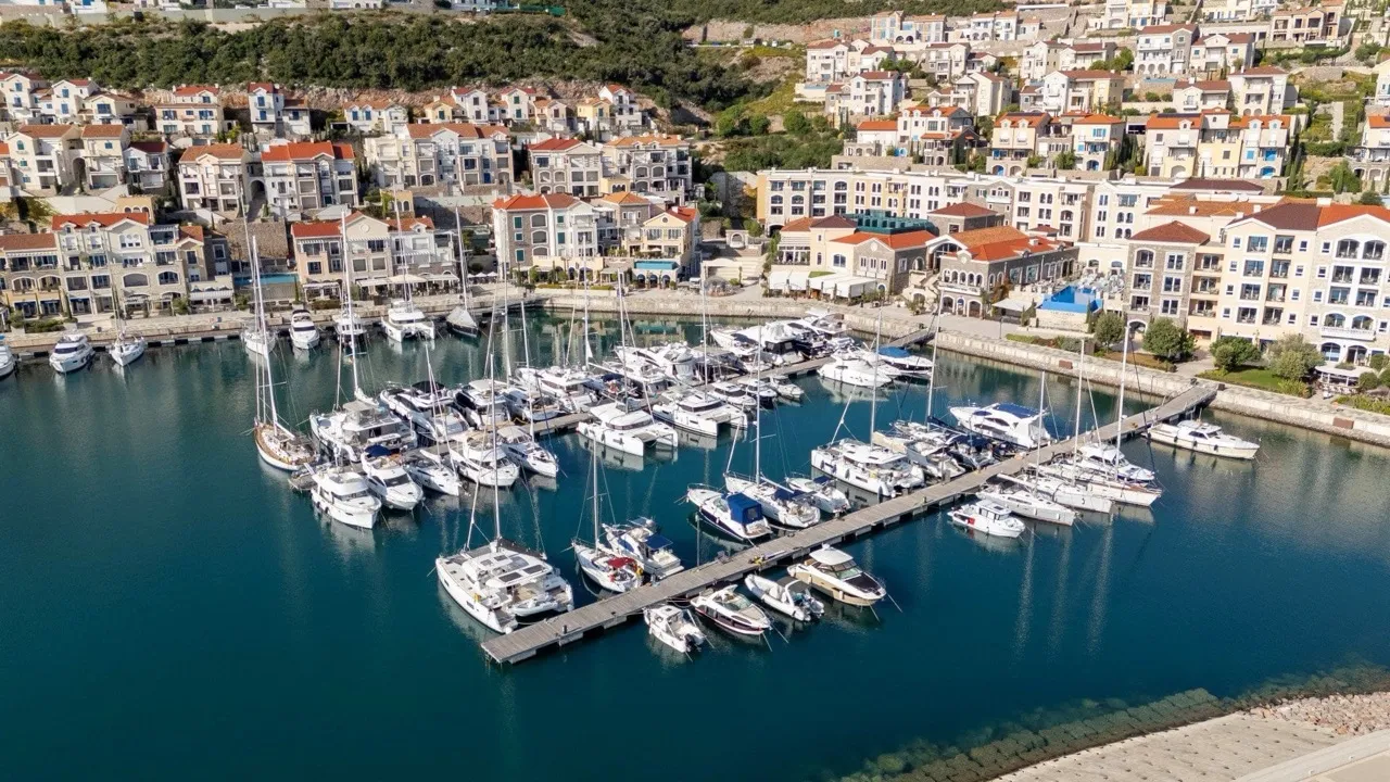 Aerial view of a marina filled with sailboats and yachts, surrounded by coastal residential buildings on a hillside.