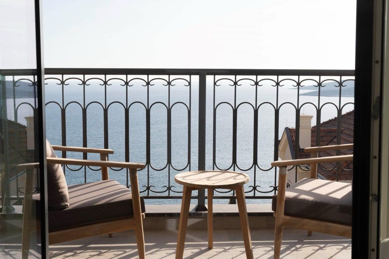 Wooden chairs and table on a balcony with an iron railing overlooking the sea.