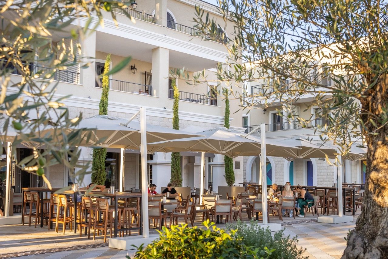 Restaurant terrace with umbrellas and tables at the Lustica Bay residential complex in Radovici, Montenegro, view of the building facades.