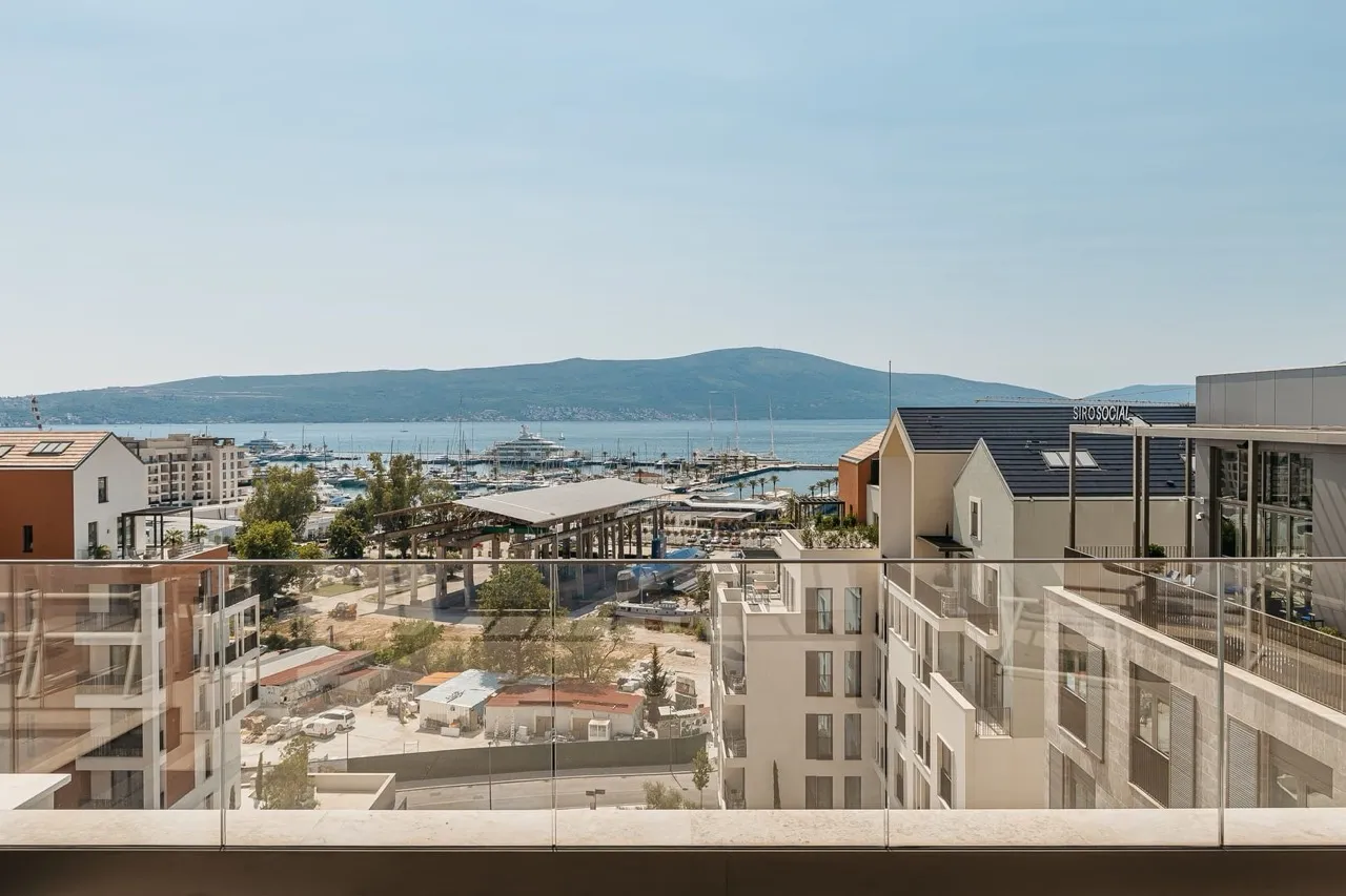 View from a balcony with a glass railing overlooking a marina and the sea.