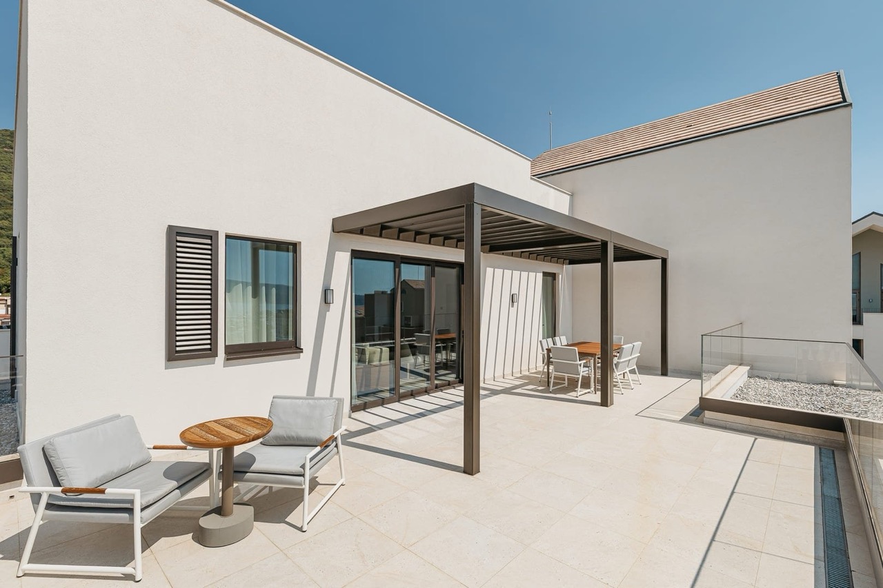 Terrace of a modern apartment in Porto Montenegro, Tivat, Montenegro: dining area under a pergola and lounge chairs.