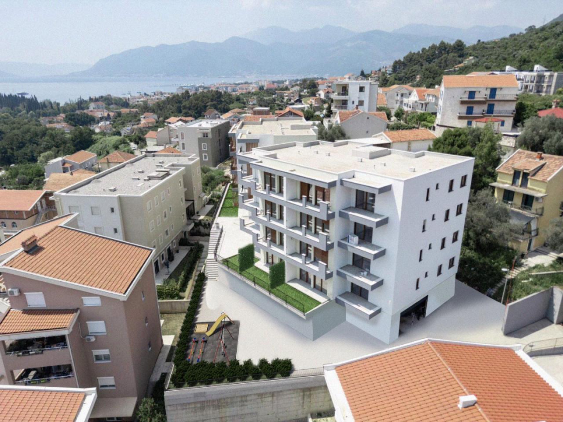 Modern residential complex with a playground in Tivat, Montenegro: aerial view of the building and the seaside.