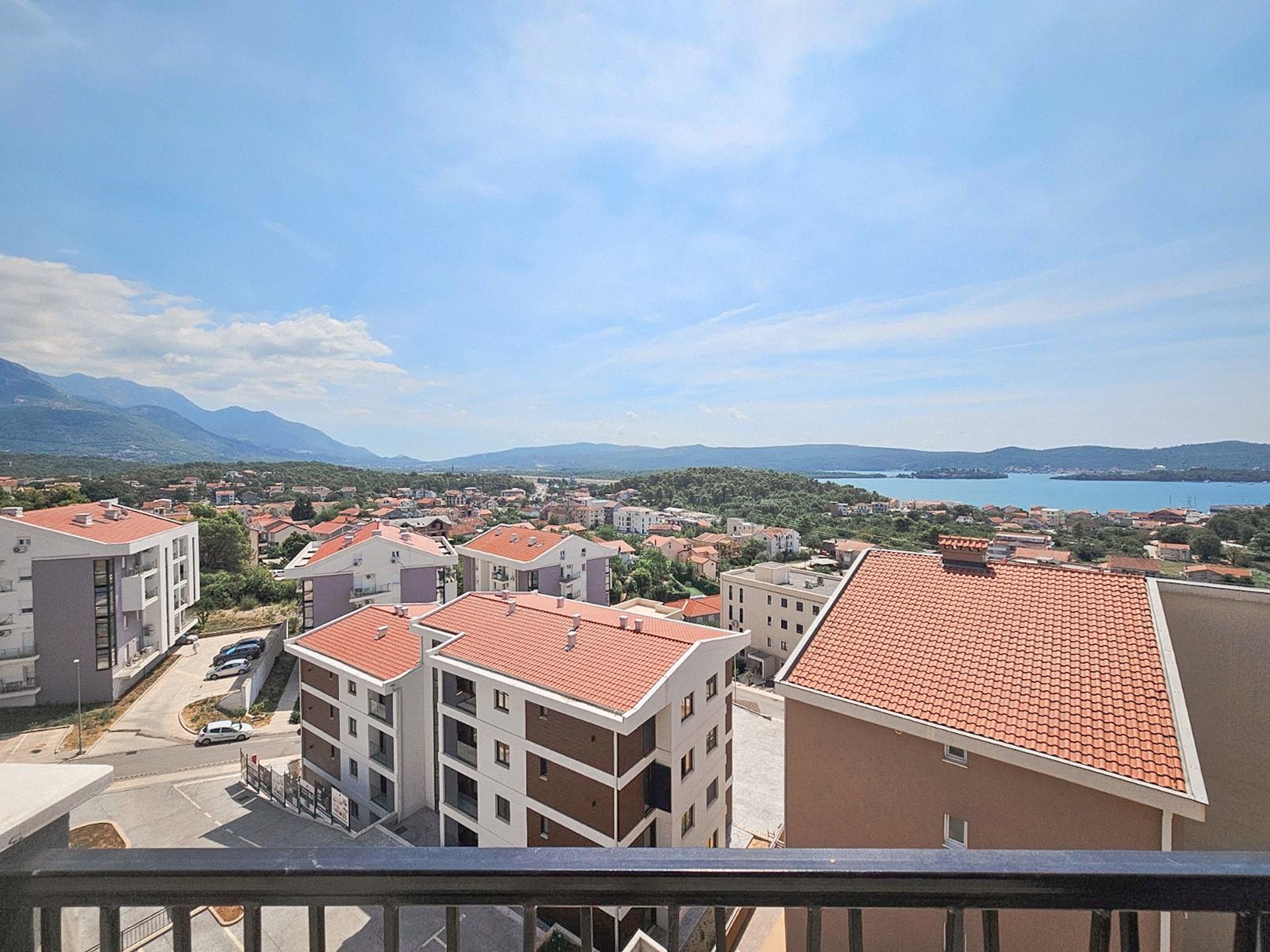 View from the apartment balcony in Tivat, Montenegro: a panorama of modern houses with tiled roofs, mountains, and the sea bay.