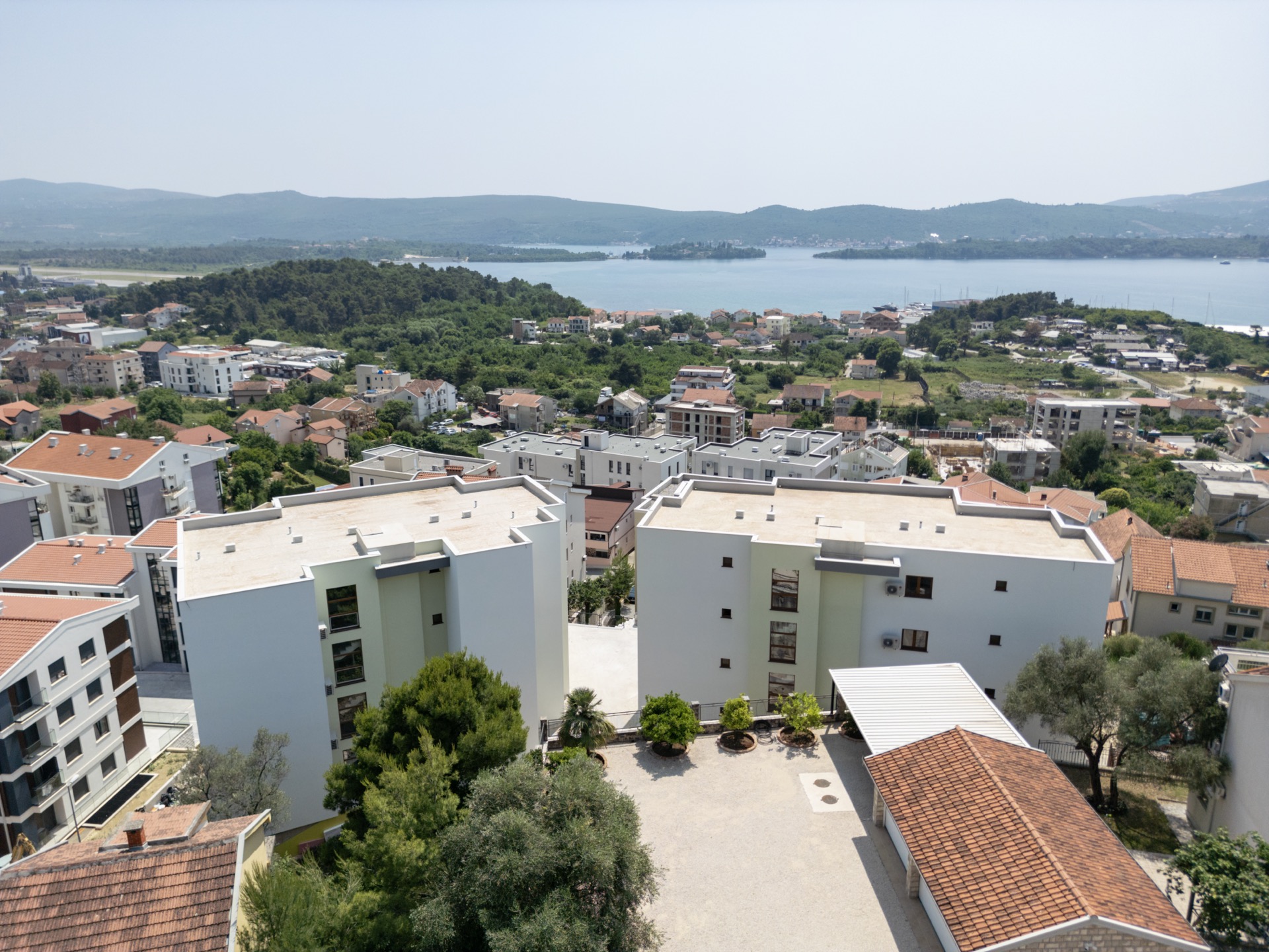 Aerial view of modern residential complexes in Tivat, Montenegro, with panoramic views of the sea and mountains.