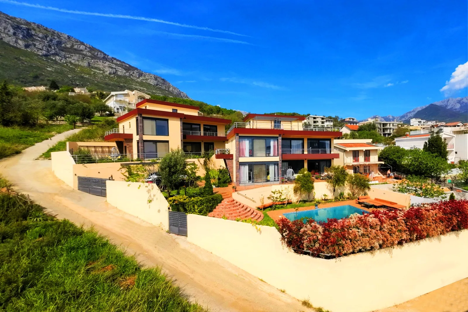 Exterior view of a modern house with a pool and garden set against mountains.