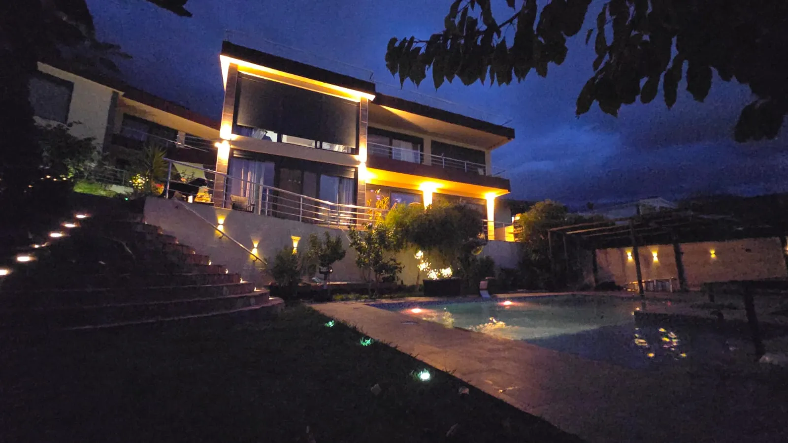 Night view of a modern two-story house with an illuminated pool and terrace.