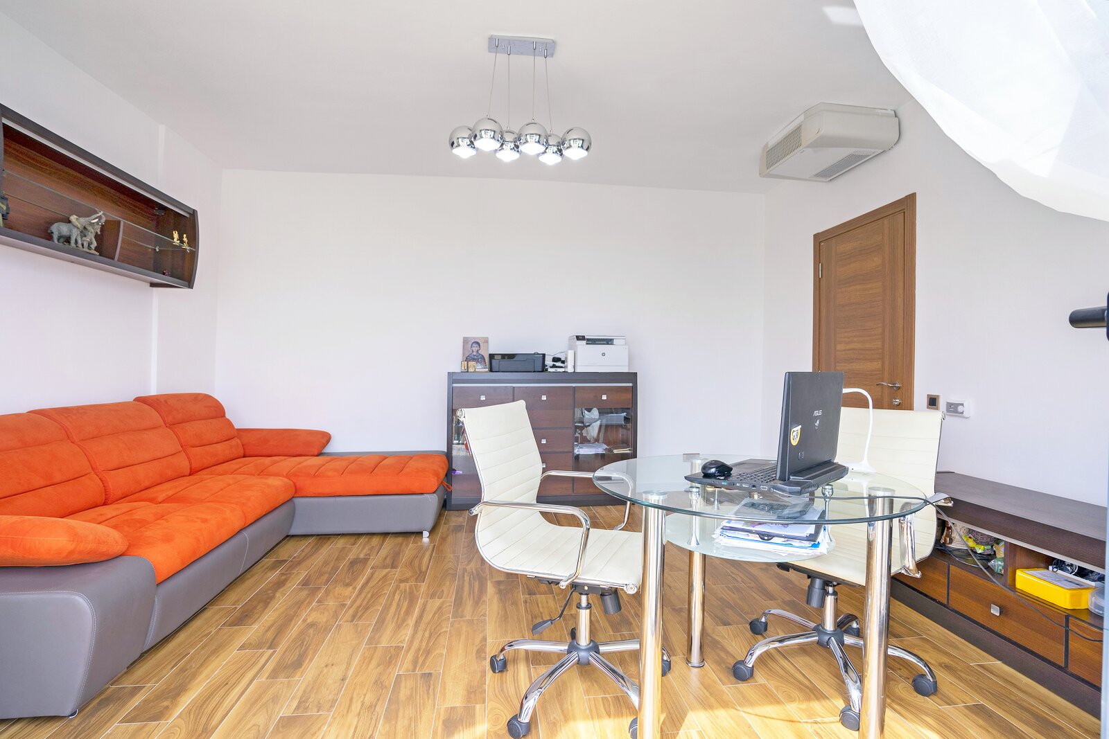 Living room with an orange sofa and workspace in a villa in Bar, Montenegro: glass table, office chairs, and laminate flooring.