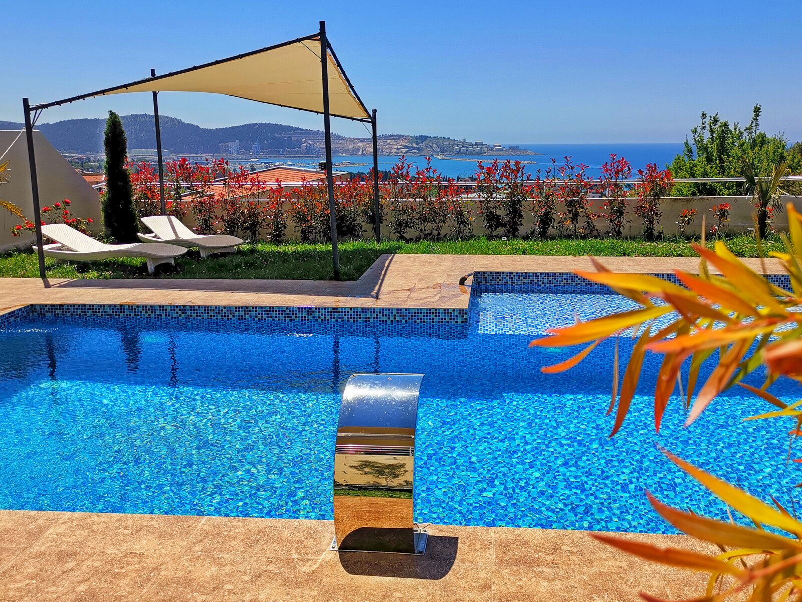 Pool with a waterfall at a villa in Bar, Montenegro: a terrace with sun loungers, a canopy, and panoramic views of the Adriatic Sea.