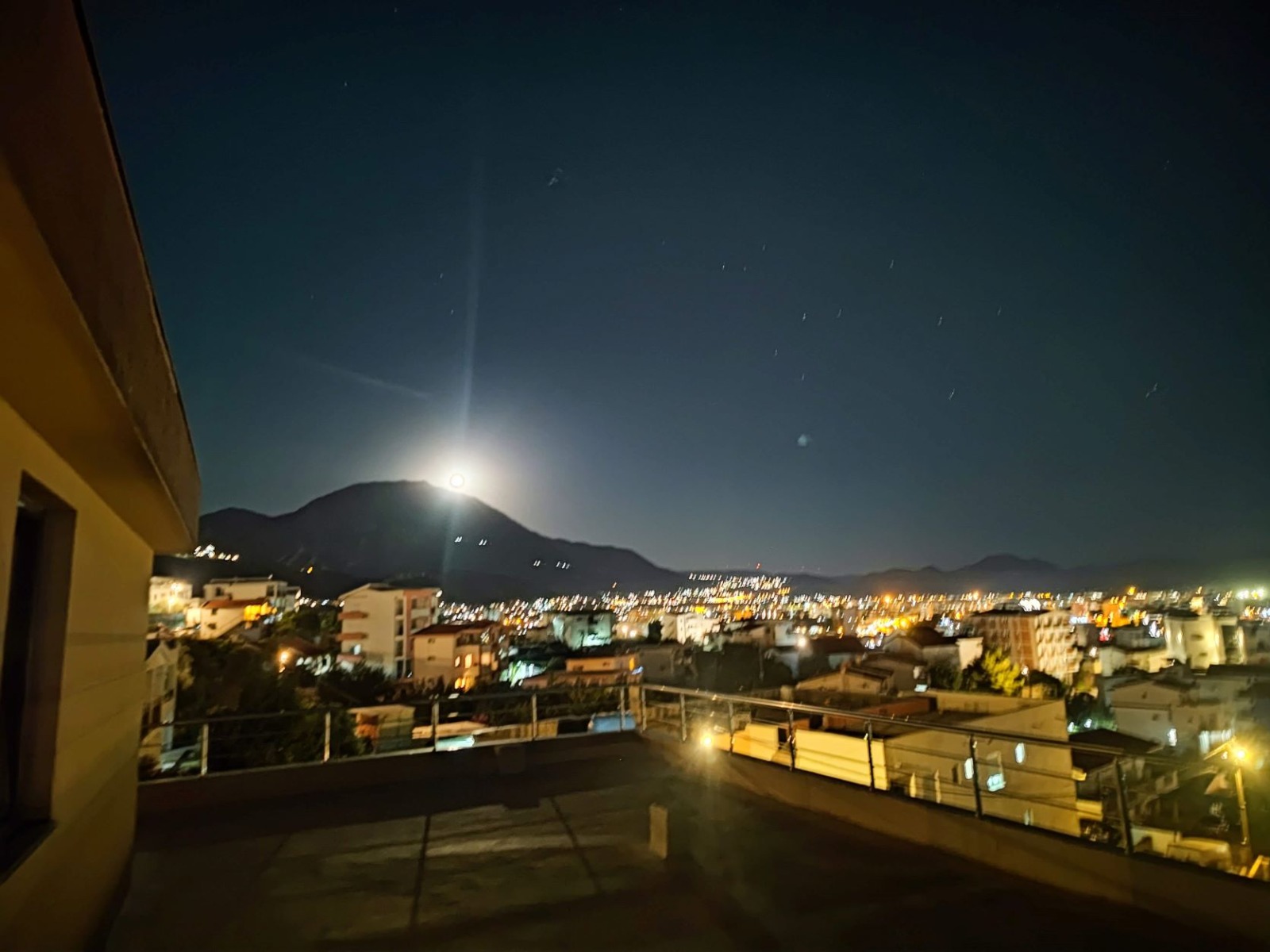 Night view from the terrace of a villa in Bar, Montenegro: a panorama of the city, house lights, and mountains under a moonlit sky.