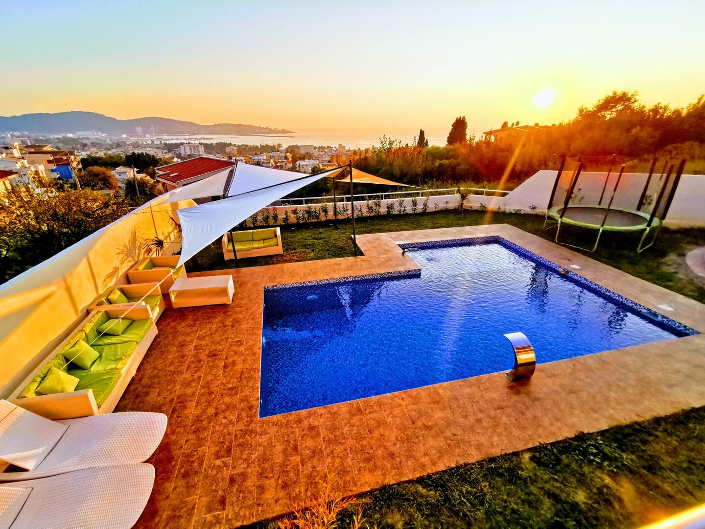 Outdoor pool at a villa in Bar, Montenegro: a relaxation area with sun loungers, a canopy, and a panoramic sea view at sunset.