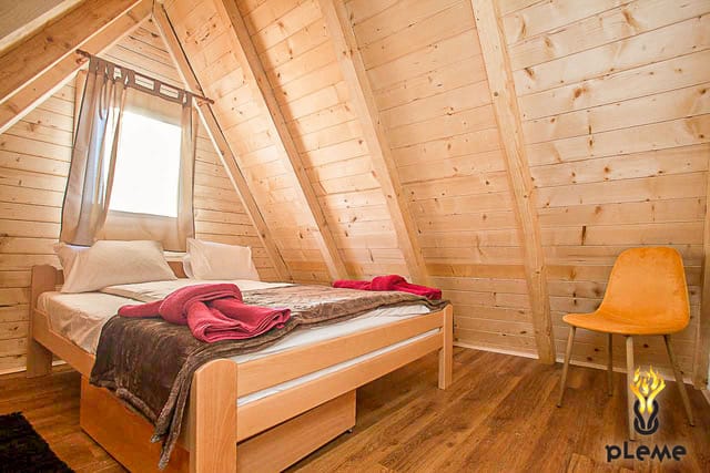 Cozy bedroom in a wooden house in Žabljak, Montenegro: a double bed, sloped walls, and a yellow chair.