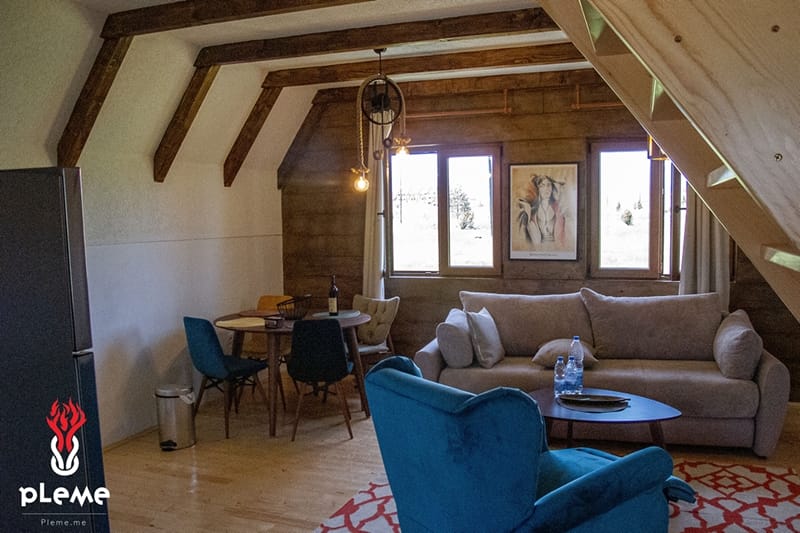 Living room in a wooden style with beams in a house complex, Žabljak, Montenegro: a soft sofa, armchair, and dining area.