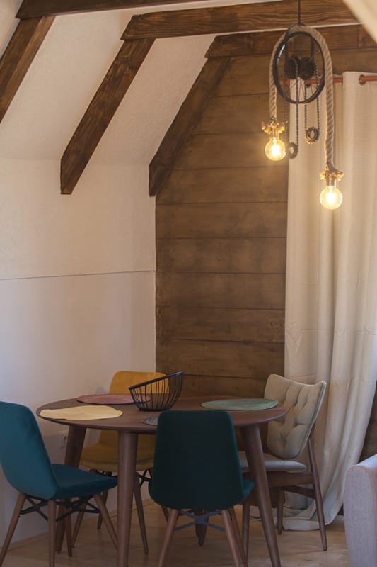 Loft-style dining area with wooden beams in a house, Žabljak, Montenegro: round table and colorful chairs.