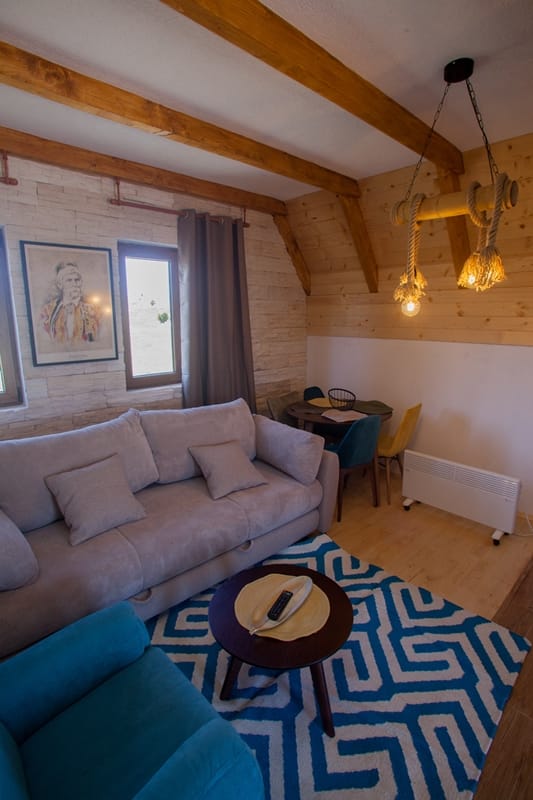 Cozy living room in a wooden house in Žabljak, Montenegro: a soft sofa, stylish decor, a beamed ceiling, and mountain views.
