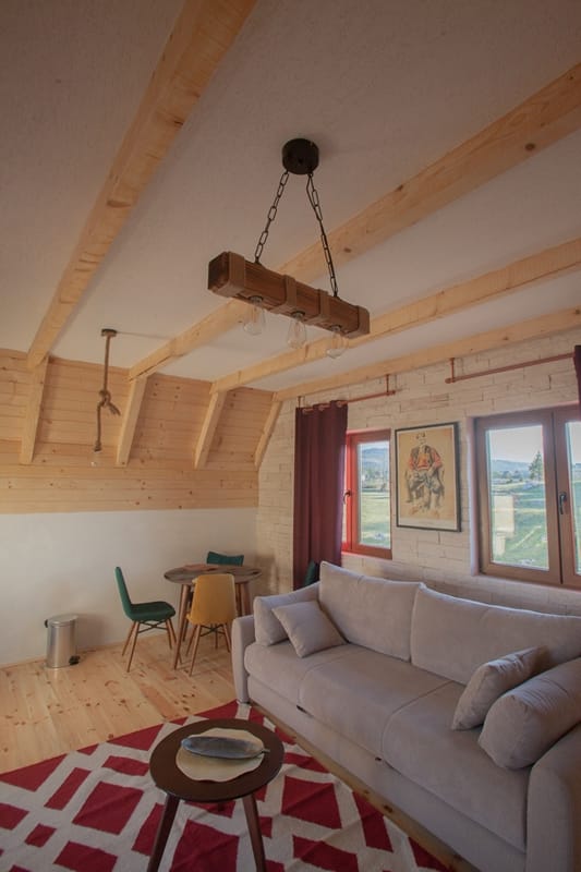 Rustic-style living room in a house in Žabljak, Montenegro: wooden beams, a light-colored sofa, dining area, and mountain views.