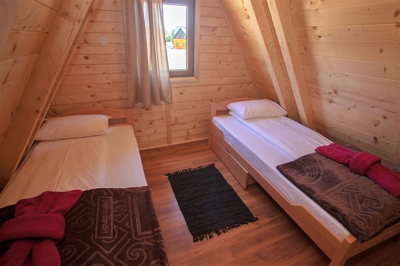 Bedroom in a wooden house in Žabljak, Montenegro: two single beds, wood finishes, and a view from the window.