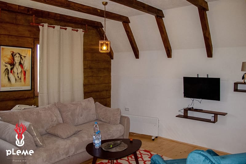Living room in a house in Žabljak, Montenegro: a cozy interior with wooden beams, a soft sofa, and a TV area.