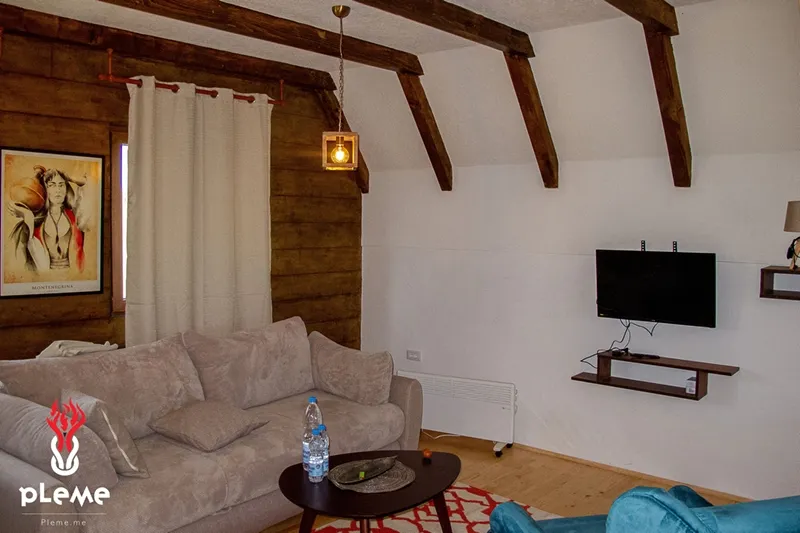 Living room featuring a beige sofa, wall-mounted TV, wooden ceiling beams, and a coffee table.