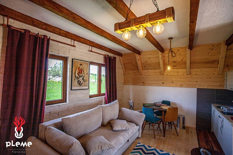Living room with beige sofa, dining table, and kitchen area under wooden ceiling beams.