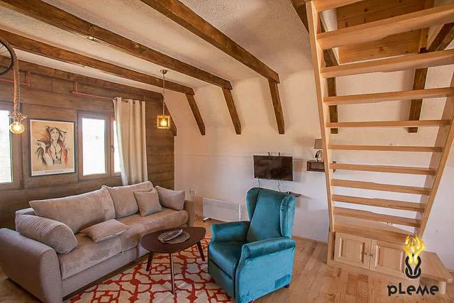 Living room with beige sofa, blue armchair, wooden ceiling beams, and a wooden staircase.