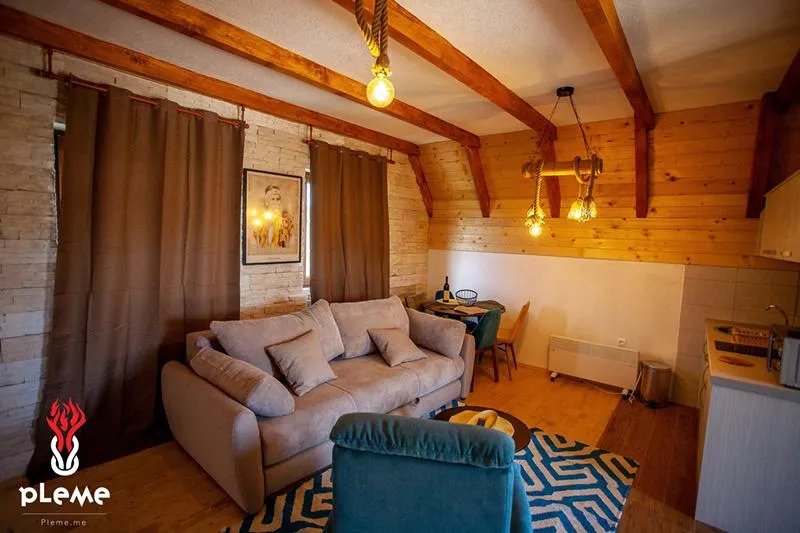 Living room featuring a beige sofa, exposed wooden ceiling beams, and a small dining area in the corner.
