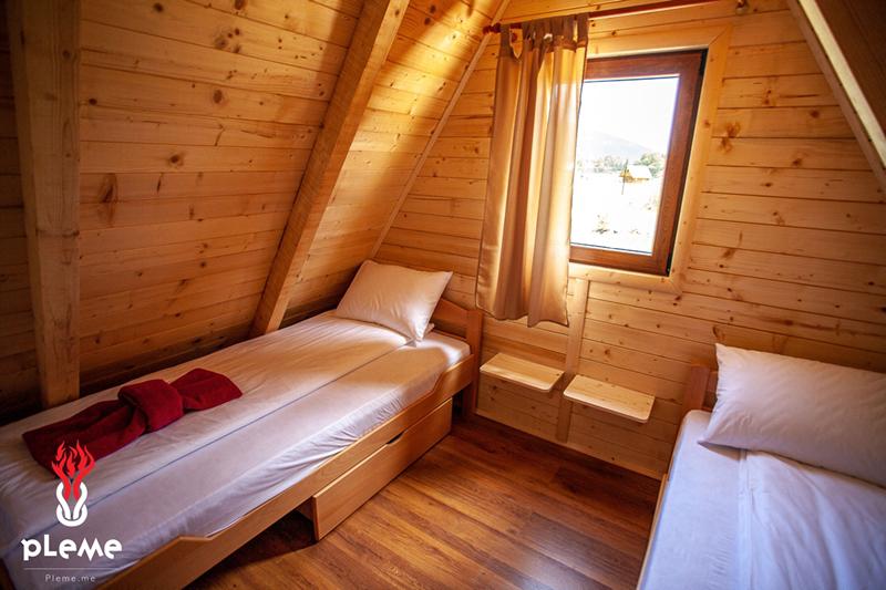 Wooden bedroom in an eco-house in Žabljak, Montenegro: two beds, sloped walls, and a mountain view from the window.