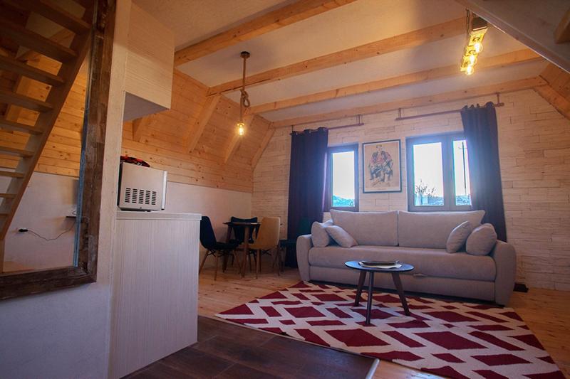 Living room in a wooden house in Žabljak, Montenegro: bright interior, soft sofa, dining area, and beamed ceiling.