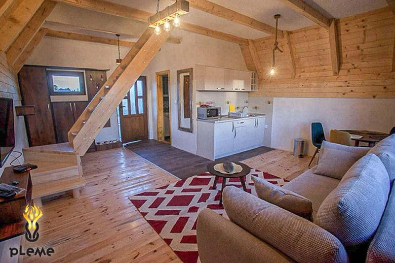 Living room with sofa, rug, and open kitchen under wooden ceiling beams.