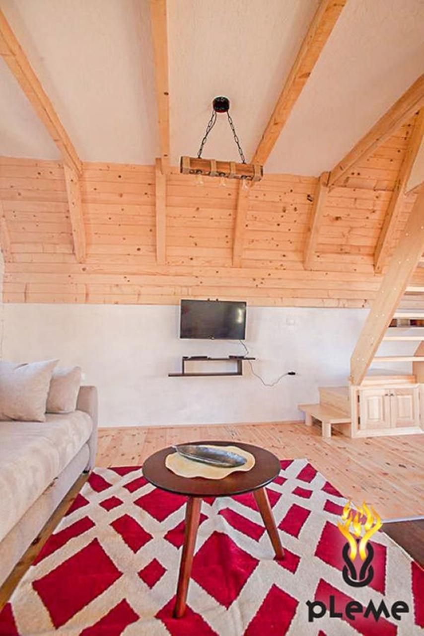 Living room in a wooden house in Žabljak, Montenegro: light wood finishes, a cozy sofa, and a staircase to the second floor.