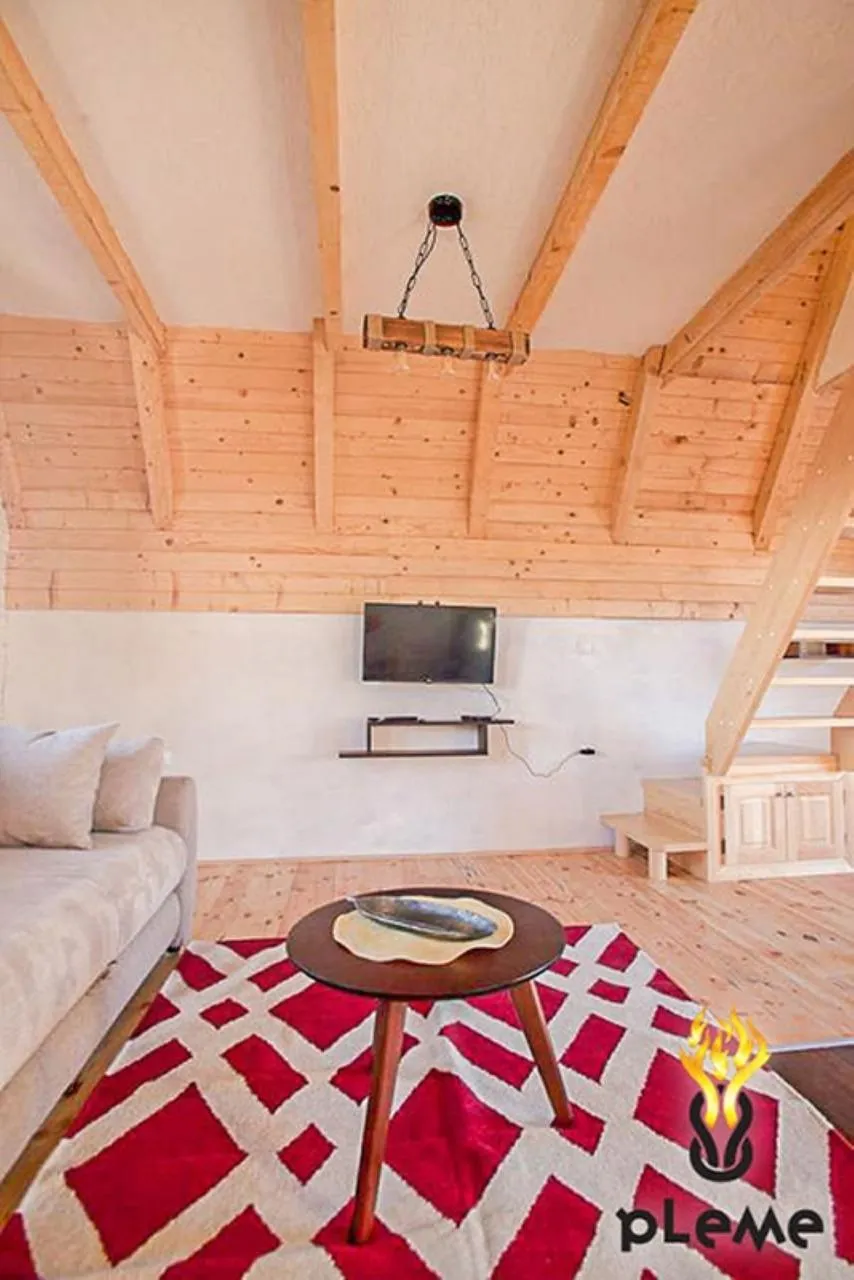 Living room with wooden beams, sofa, coffee table, and wall-mounted TV on wood paneling.