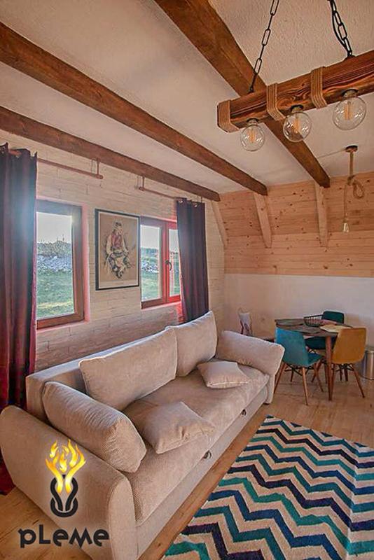 Rustic-style living room with wooden beams in a house, Žabljak, Montenegro: a soft sofa, dining area, and a view from the windows.