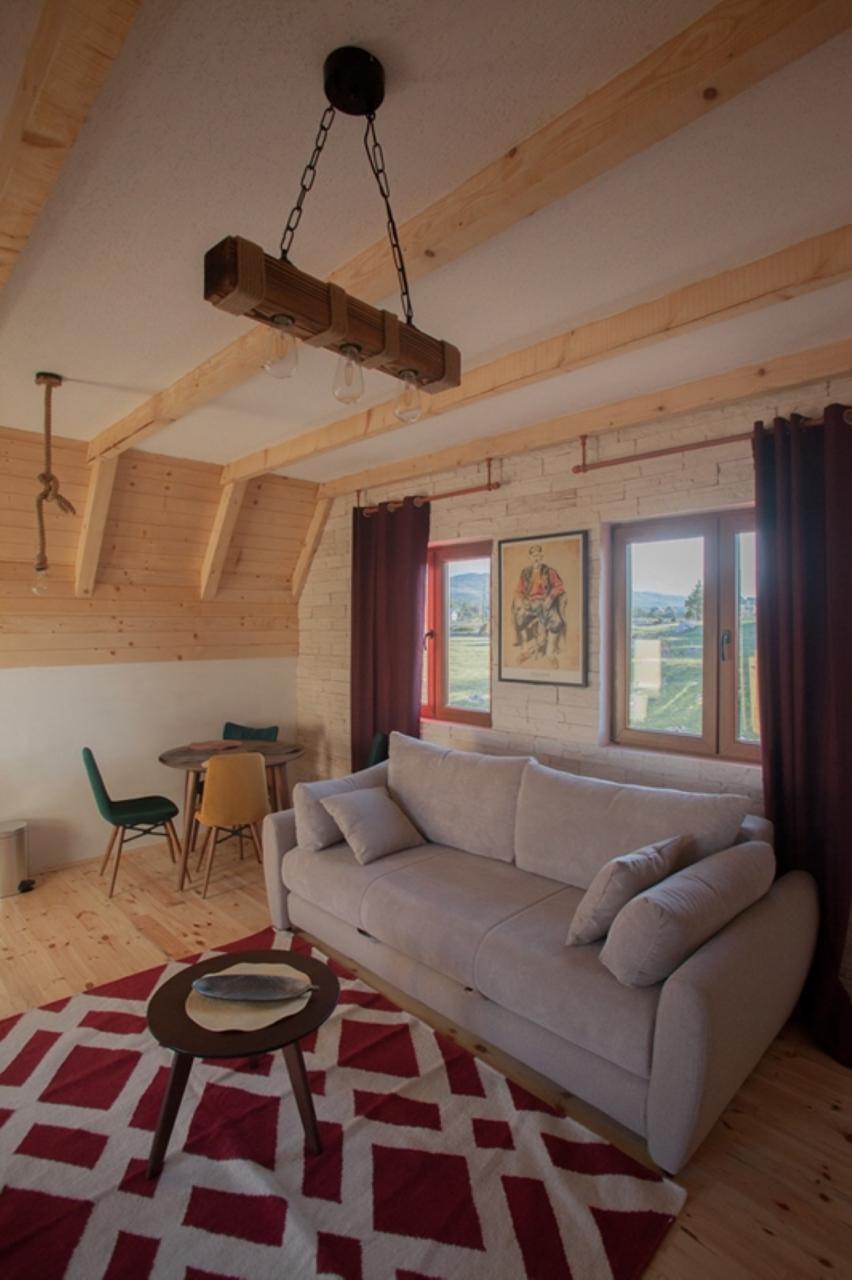 Cozy living room in a wooden house in Žabljak, Montenegro: a light sofa, beam ceiling, and mountain view.