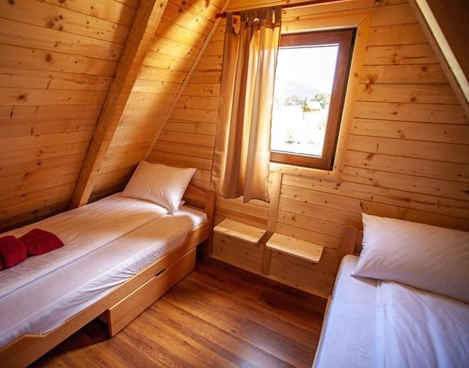 Bedroom in a wooden house in Žabljak, Montenegro: two beds, wood finishes, and a mountain view from the window.