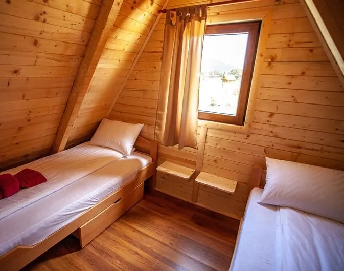 Wooden attic room with two single beds, a window, and curtains under a sloped ceiling.