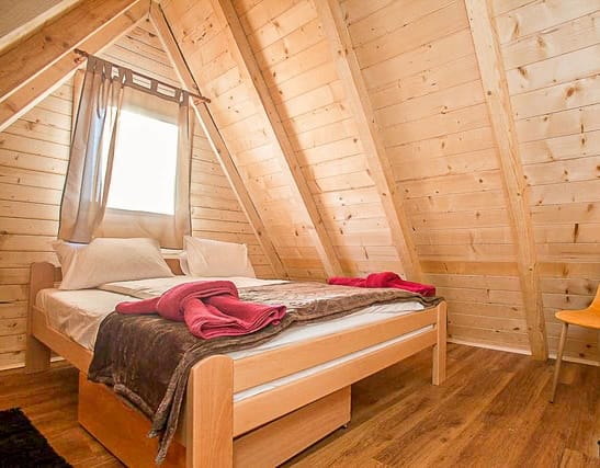 Cozy bedroom in a wooden house in Žabljak, Montenegro: double bed, sloped ceiling, wood finish.